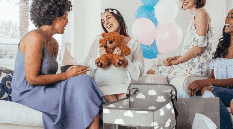 Amigas jugando con la futura mamá en un baby shower con globos y un osito de peluche