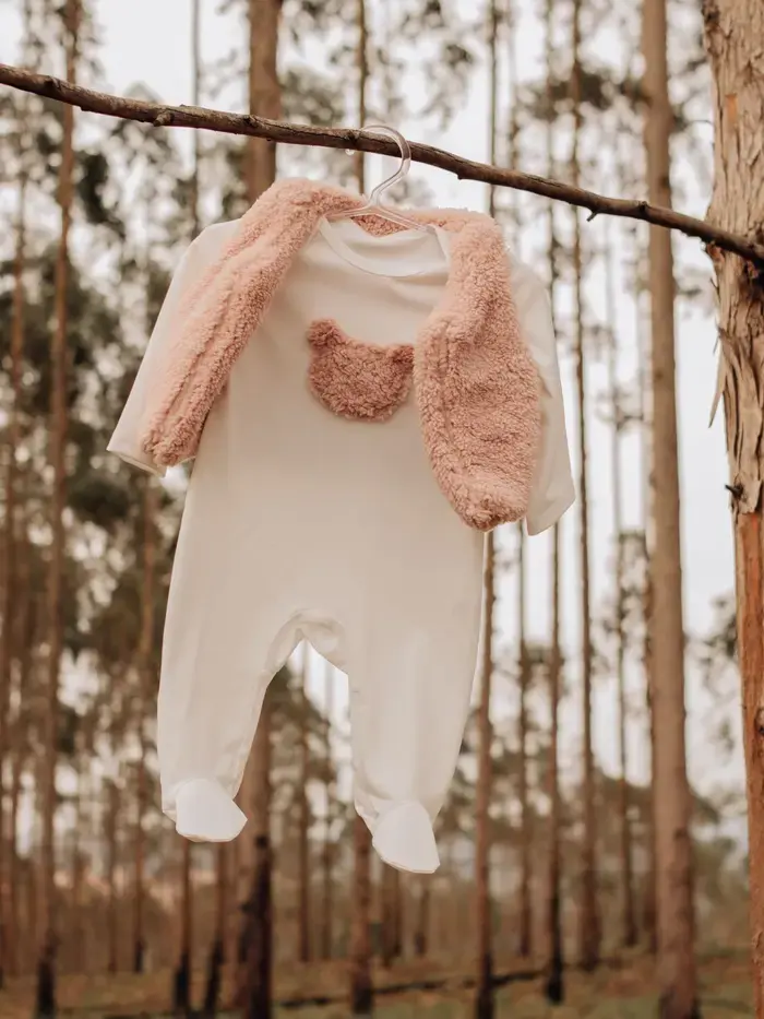 Pelele de bebé blanco con chaleco de borrego colgado de una rama en el bosque
