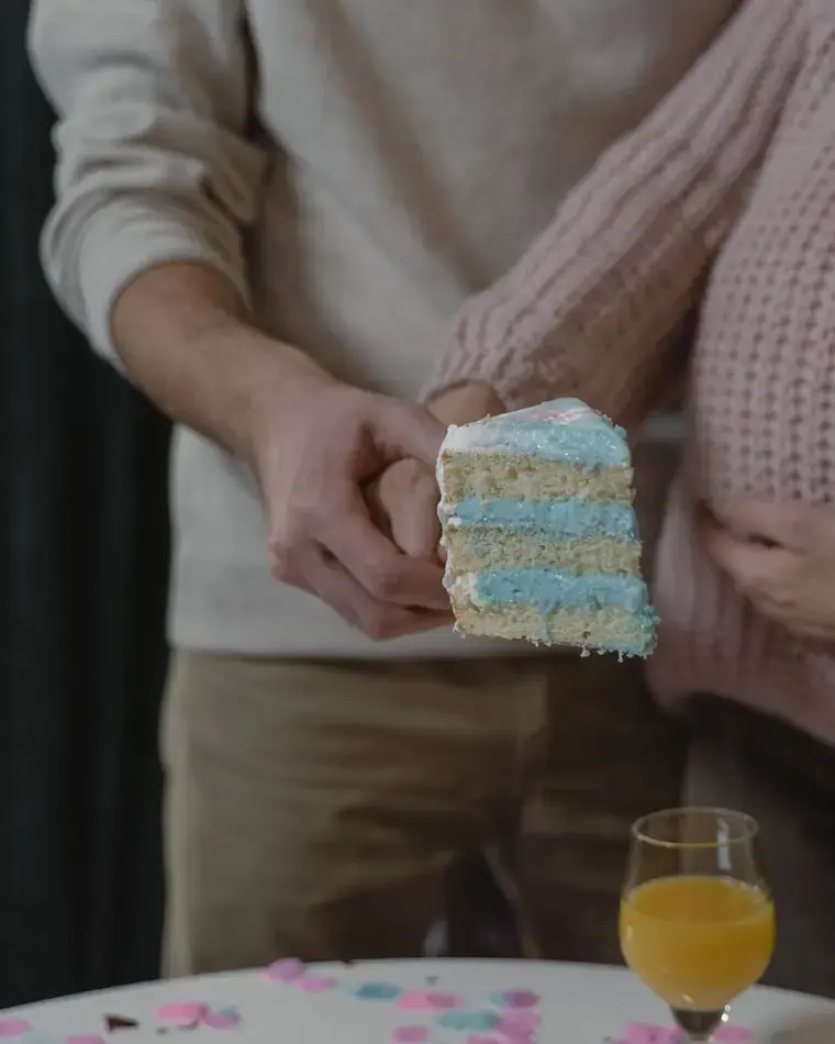 Futura mamá con jersey de punto sujetando su barriga mientras su pareja corta la tarta de revelación