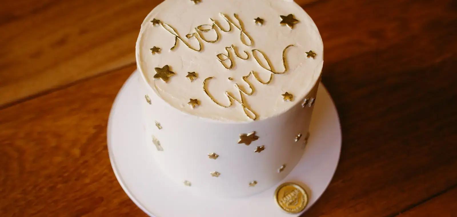 Tarta blanca con estrellas doradas y la frase boy or girl sobre una mesa de madera